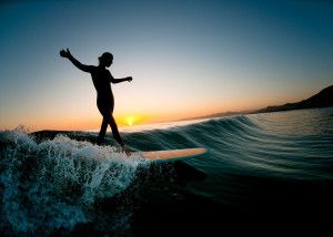 впевнений серфер дівчина на хвилі із заходом сонця на тлі